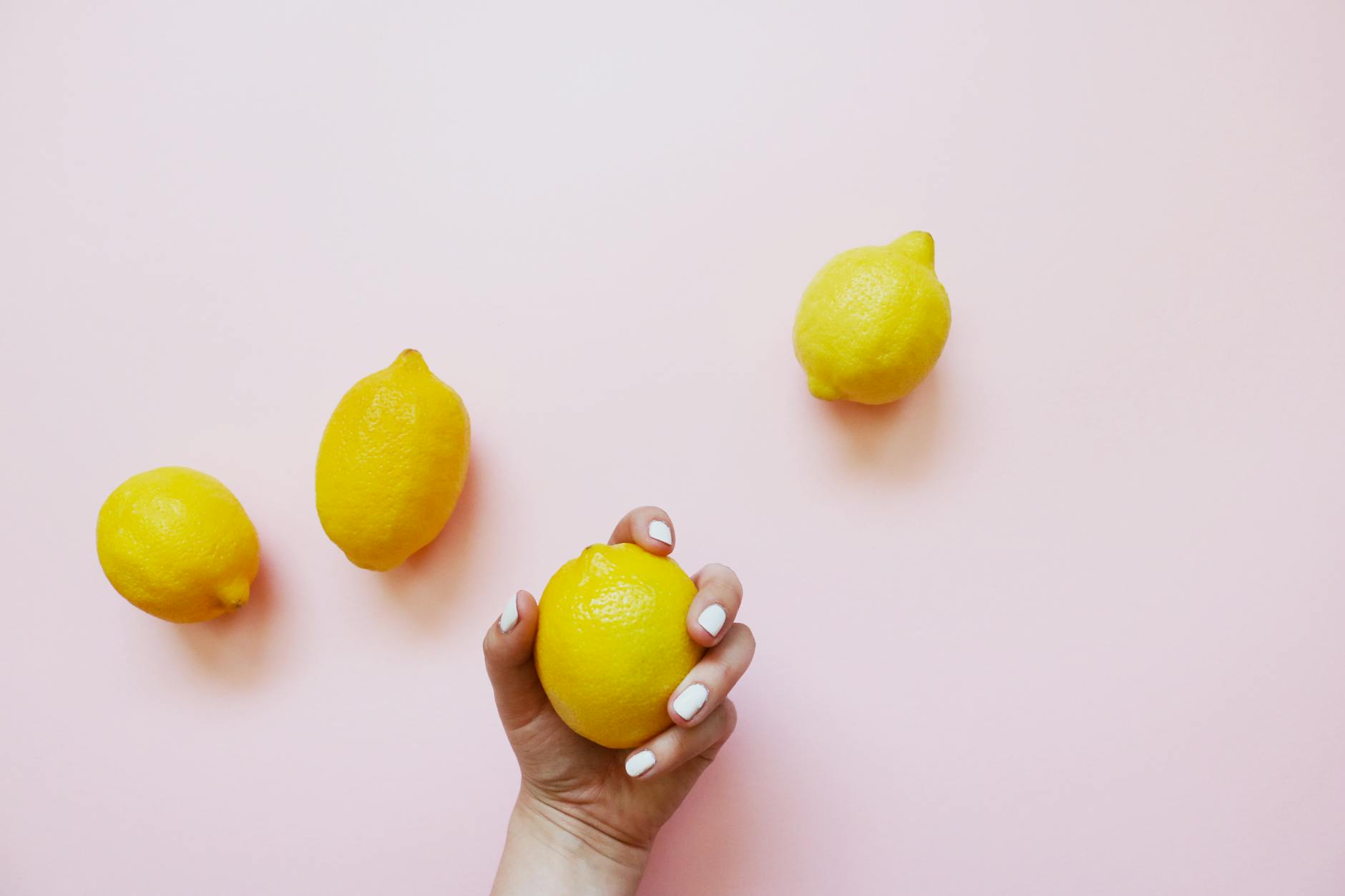 A hand holding a lemon on a soft pink background, symbolizing the gentle approach lemon vibrators take to sensitive post-menopausal tissue