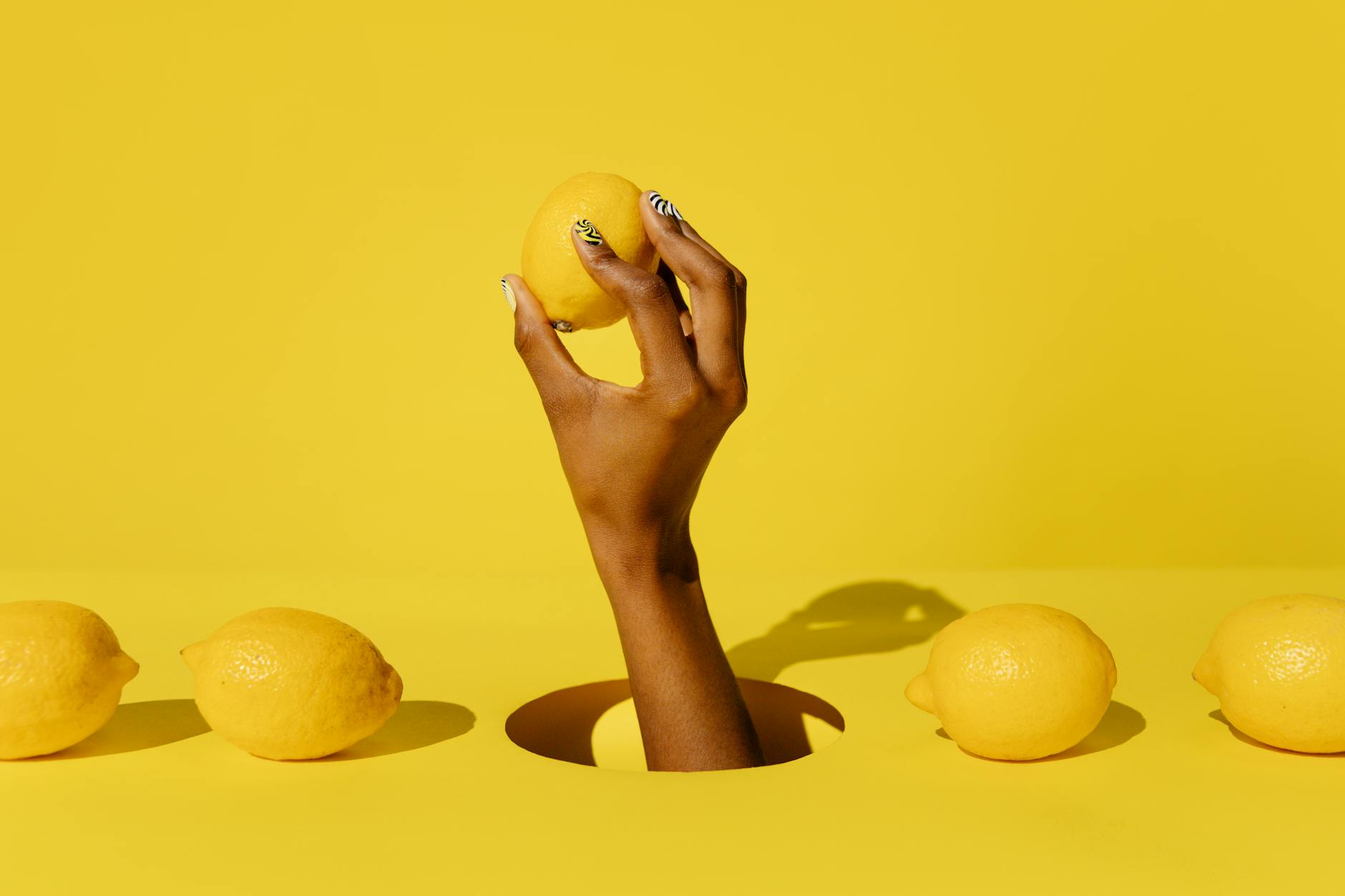A hand holding a fresh lemon against a bright yellow background, symbolizing the bold, refreshing energy of solo pleasure.