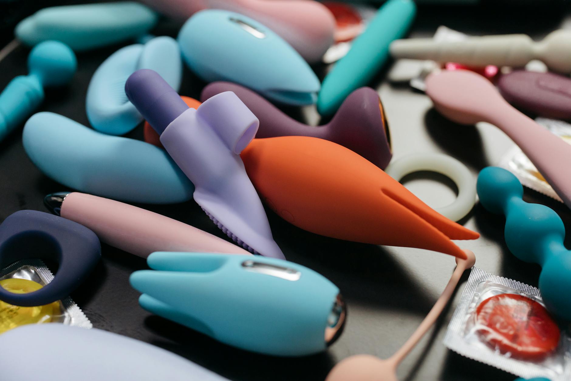 Woman holding blue and pink silicone clitoral vibrators in thoughtful contemplation
