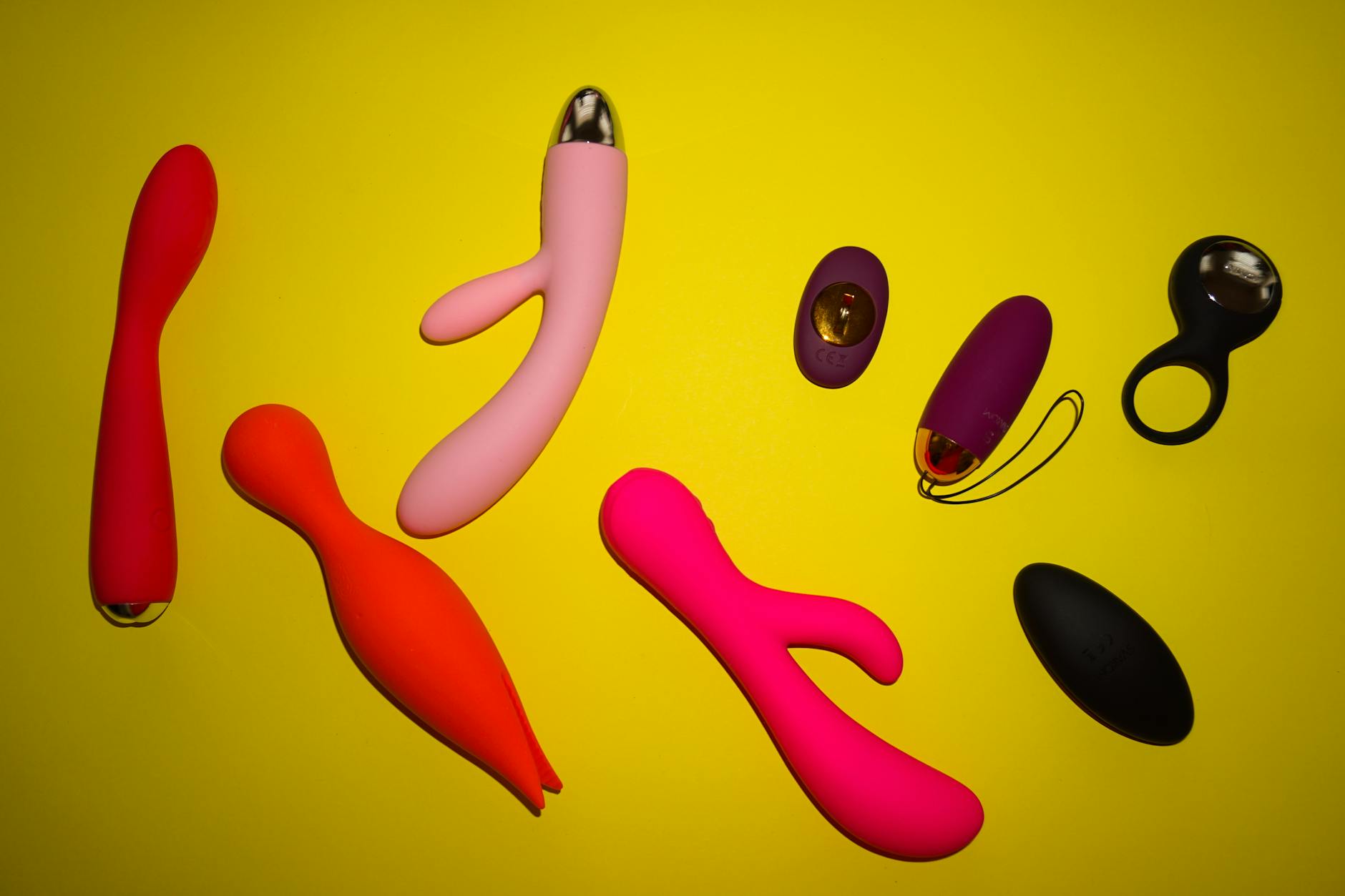 Vibrant arrangement of colorful sex toys on a bright yellow surface, showcasing diversity in adult toy design