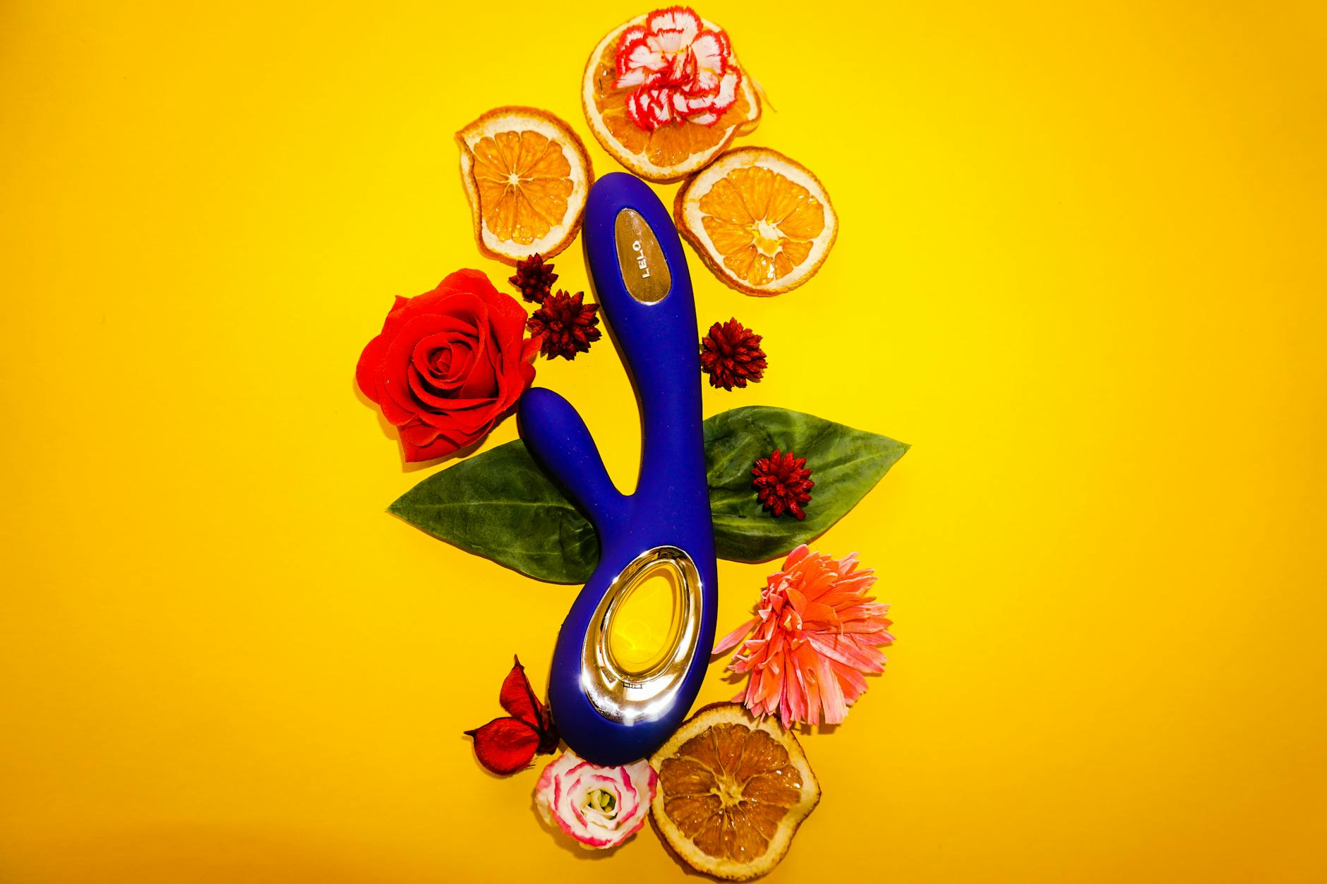 Blue vibrator surrounded by flowers on yellow background, representing pleasure and vitality