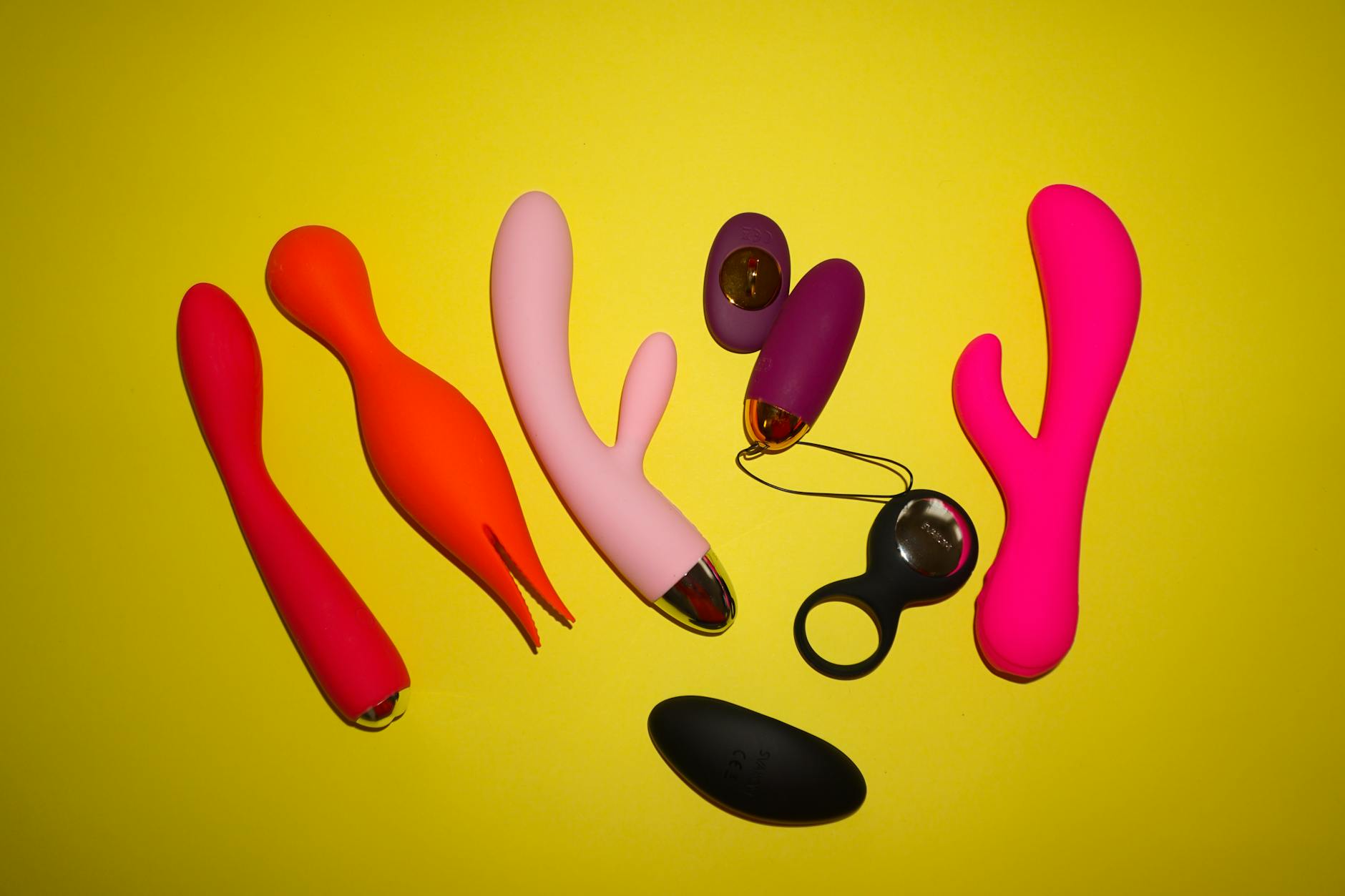 Colorful clitoral vibrators and wellness tools arranged on a bright yellow background